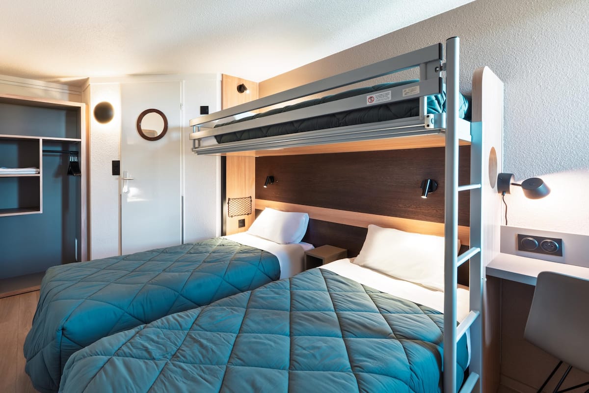 Een kleine kamer met twee stapelbedden, een bureau en een kledingkast.