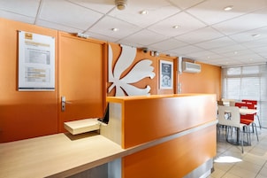 A reception area with a wooden counter, a bulletin board with a notice, and a seating area with tables and chairs.