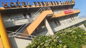 Un hôtel avec une enseigne indiquant « HÔTEL PREMIÈRE CLASSE » et une autre annonçant un service de livraison de pizzas gratuit.