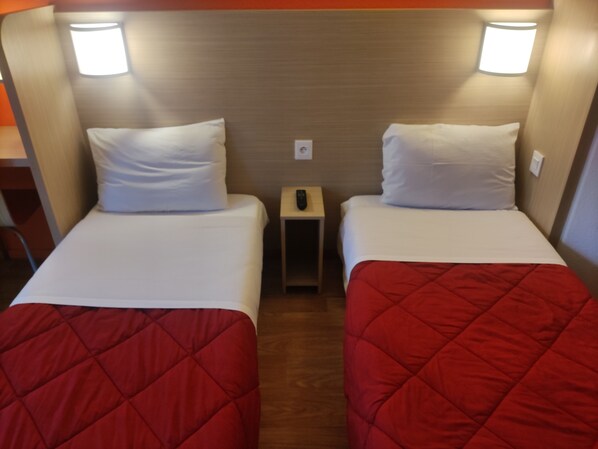 A room with two beds, each with white bedding and a red quilted cover. There are two wall-mounted lights above each bed, and a small bedside table with a remote control. - Hotel Première Classe Vannes (Vannes)