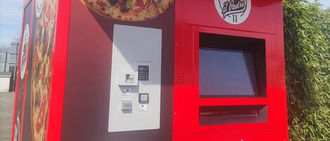 A red food vending machine with a pizza advertisement, a ticket purchase area, and a suggestion email address.