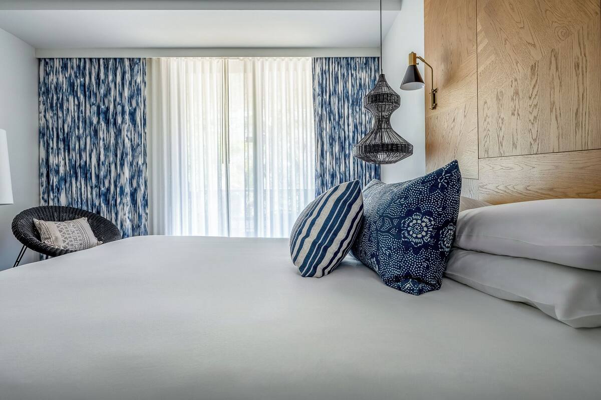 A modern hotel room with a large bed, a wicker chair, and a wooden headboard.