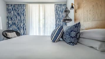 Moderni hotellihuone, jossa on suuri sänky, rottinkituoli ja puinen pääty.
