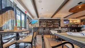 A modern bar area with seating, a television screen, and a bar stocked with bottles.