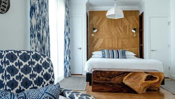 Quarto de hotel moderno com uma cama grande, cabeceira de madeira, poltrona estampada e um banco de madeira exclusivo.