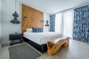 Un dormitorio moderno con una cama grande, mesitas de noche, un banco de madera y un amplio ventanal con cortinas.