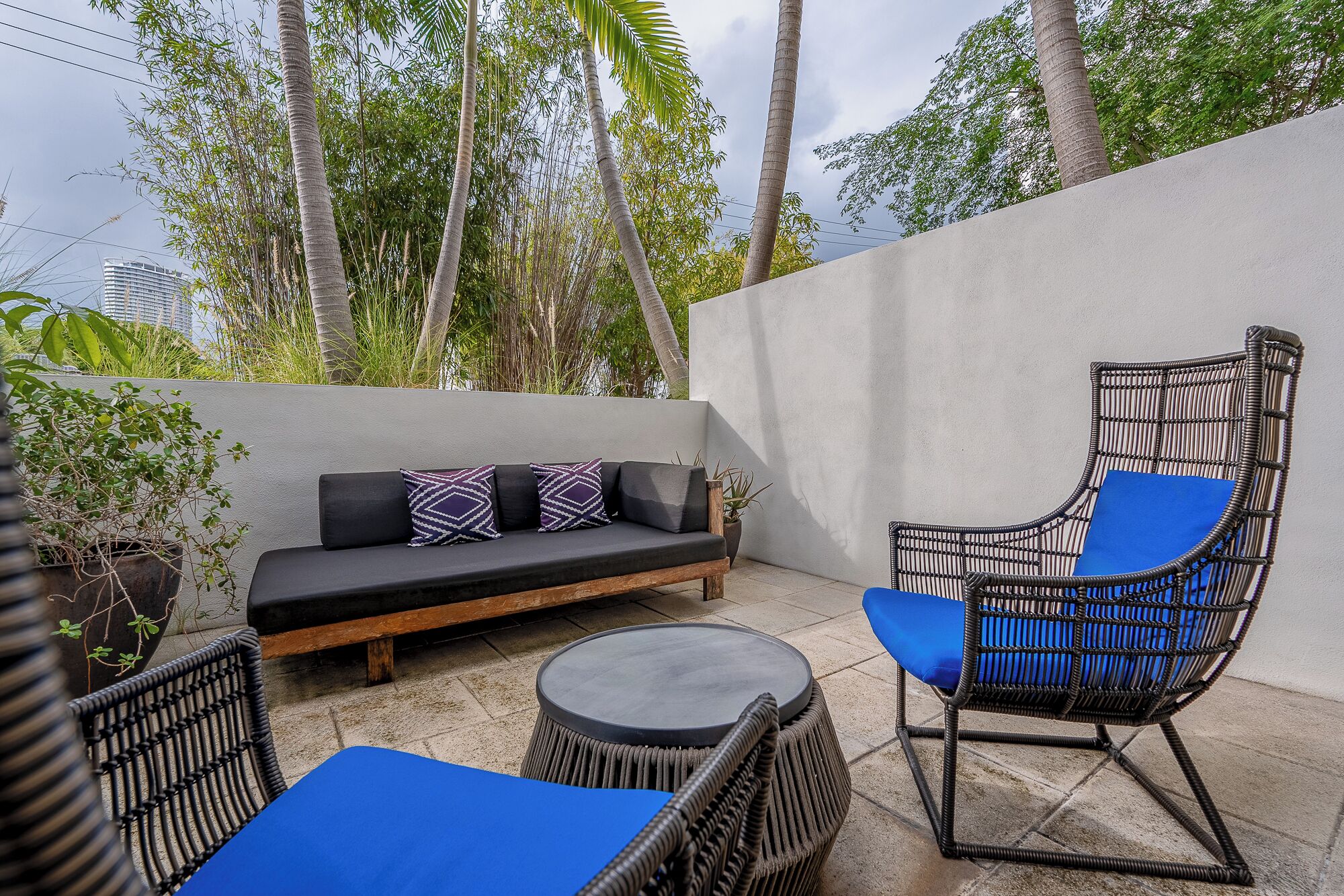 A patio with a sofa, a wicker chair, and a round table.