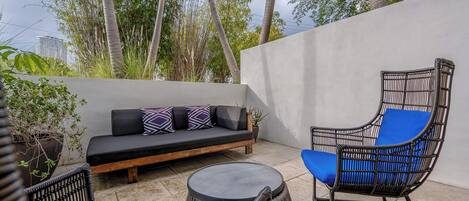 A patio with a sofa, a wicker chair, and a round table.