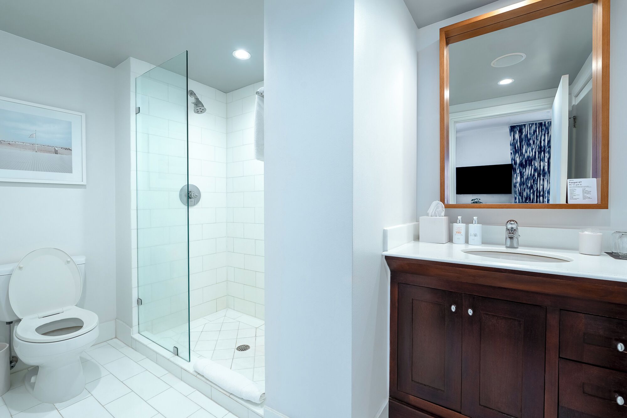 Une salle de bain moderne avec une douche à parois de verre, des toilettes, un meuble-lavabo avec un miroir et un tableau encadré au mur.