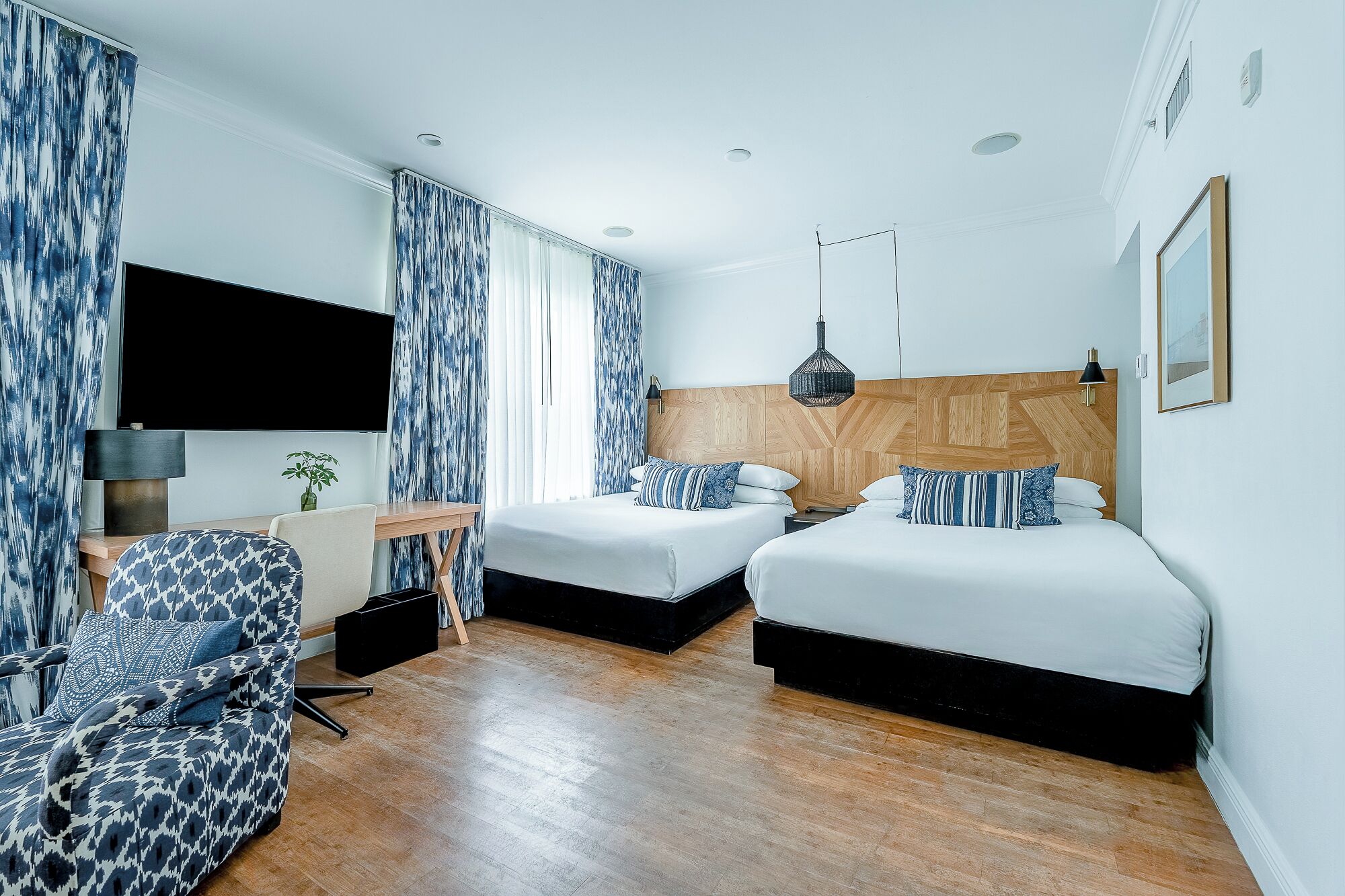 A hotel room with two beds, a desk, a chair, and a TV.