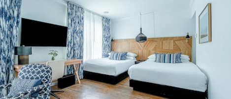 A hotel room with two beds, a desk, a chair, and a TV.
