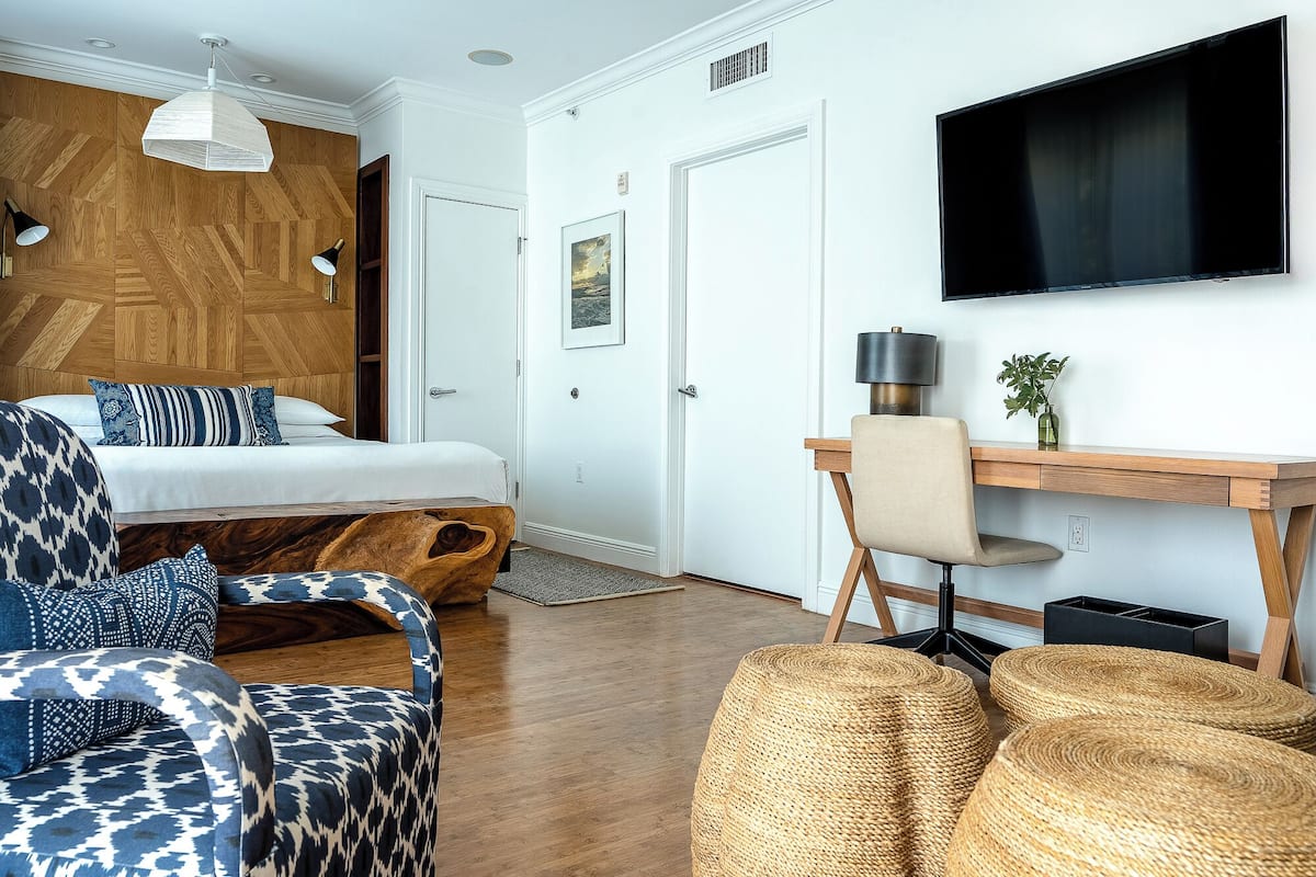 A modern hotel room with a bed, a desk, a chair, a television, and a large window.
