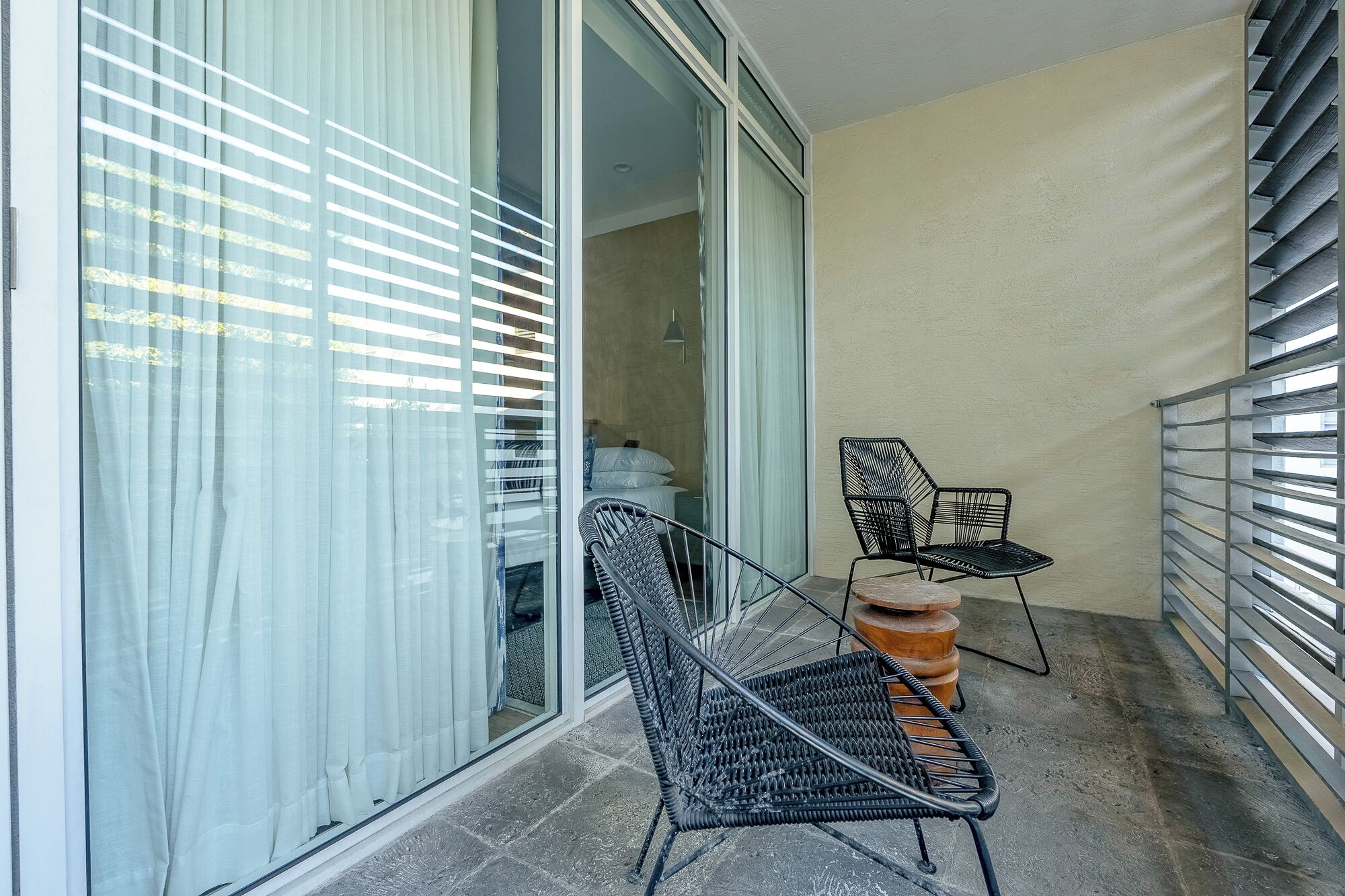 A balcony with two wicker chairs, a small table, and a sliding glass door leading to a room.