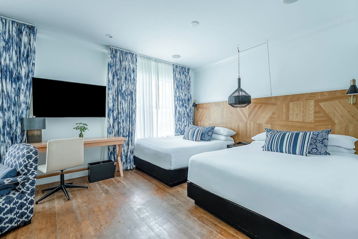A hotel room with two beds, a desk with a chair, a TV, and a hanging light fixture.