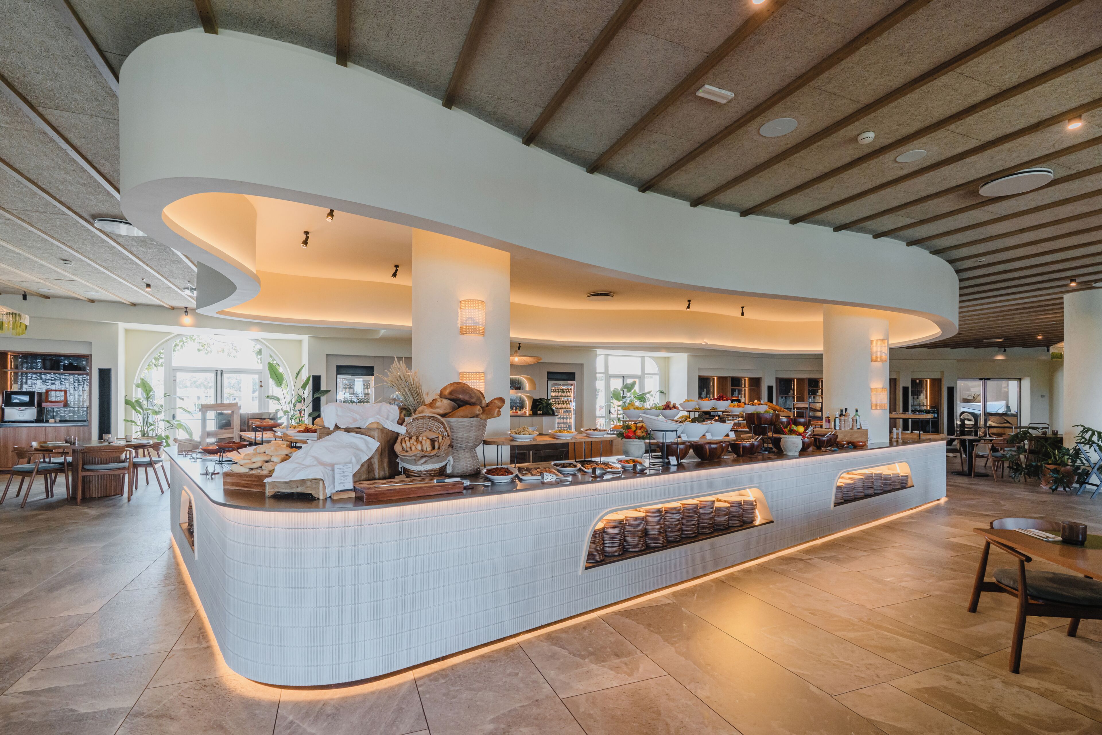 A modern hotel lobby with a curved reception desk, seating area, and a dining space.