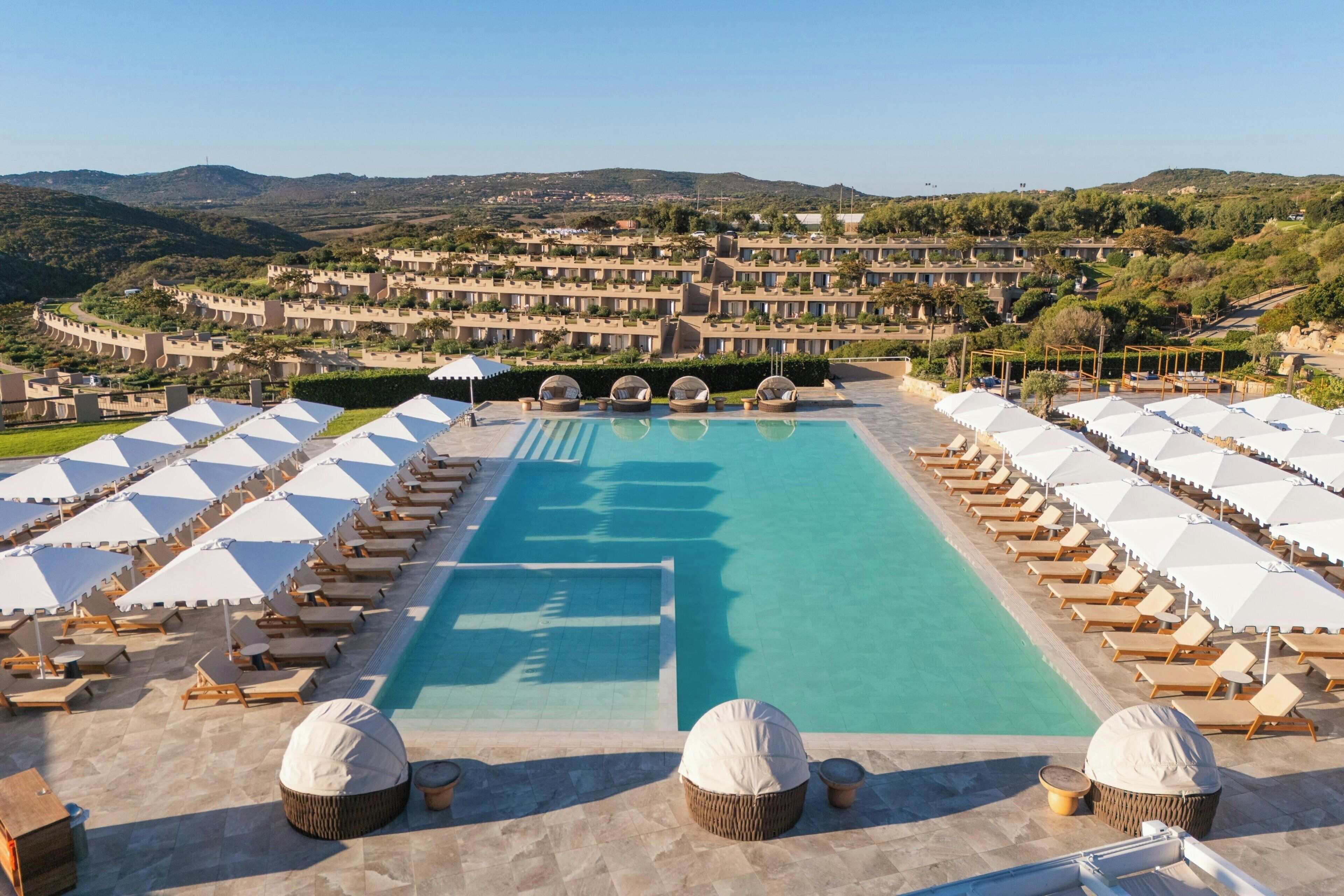 Un complexe hôtelier doté d’une grande piscine, de chaises longues et offrant une vue sur les collines environnantes.