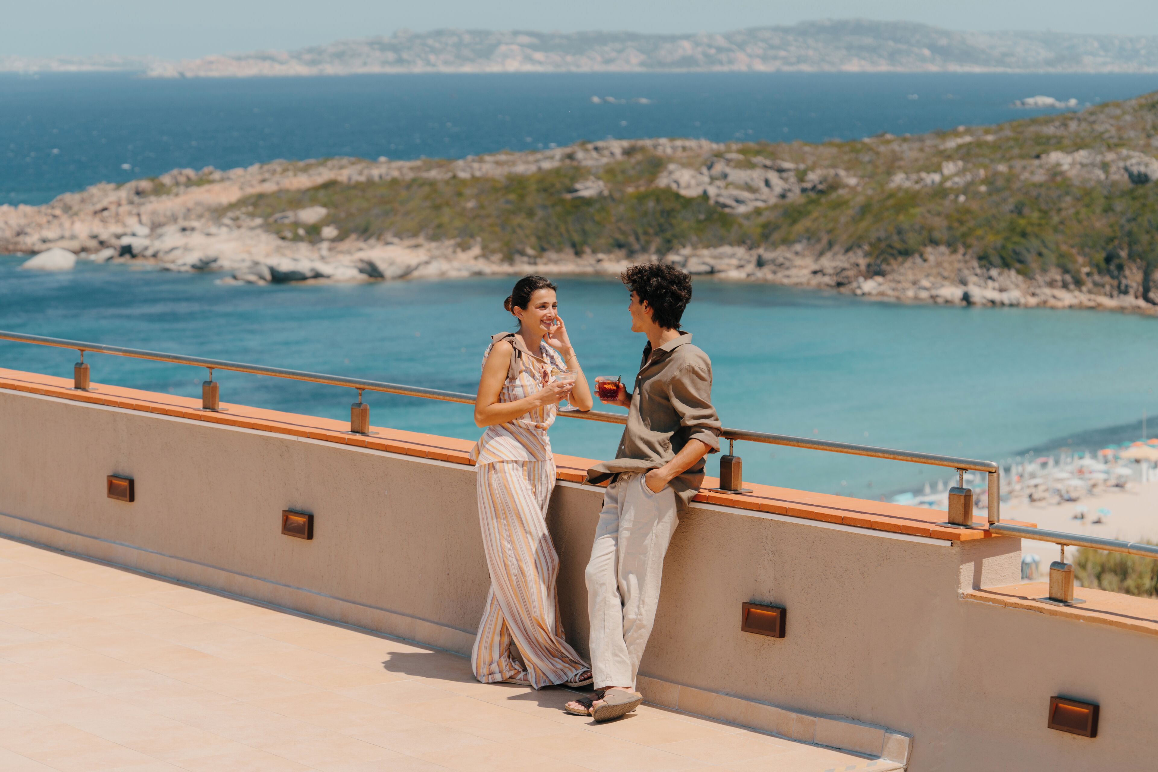 Una pareja parada en un balcón con vistas a un paisaje costero.