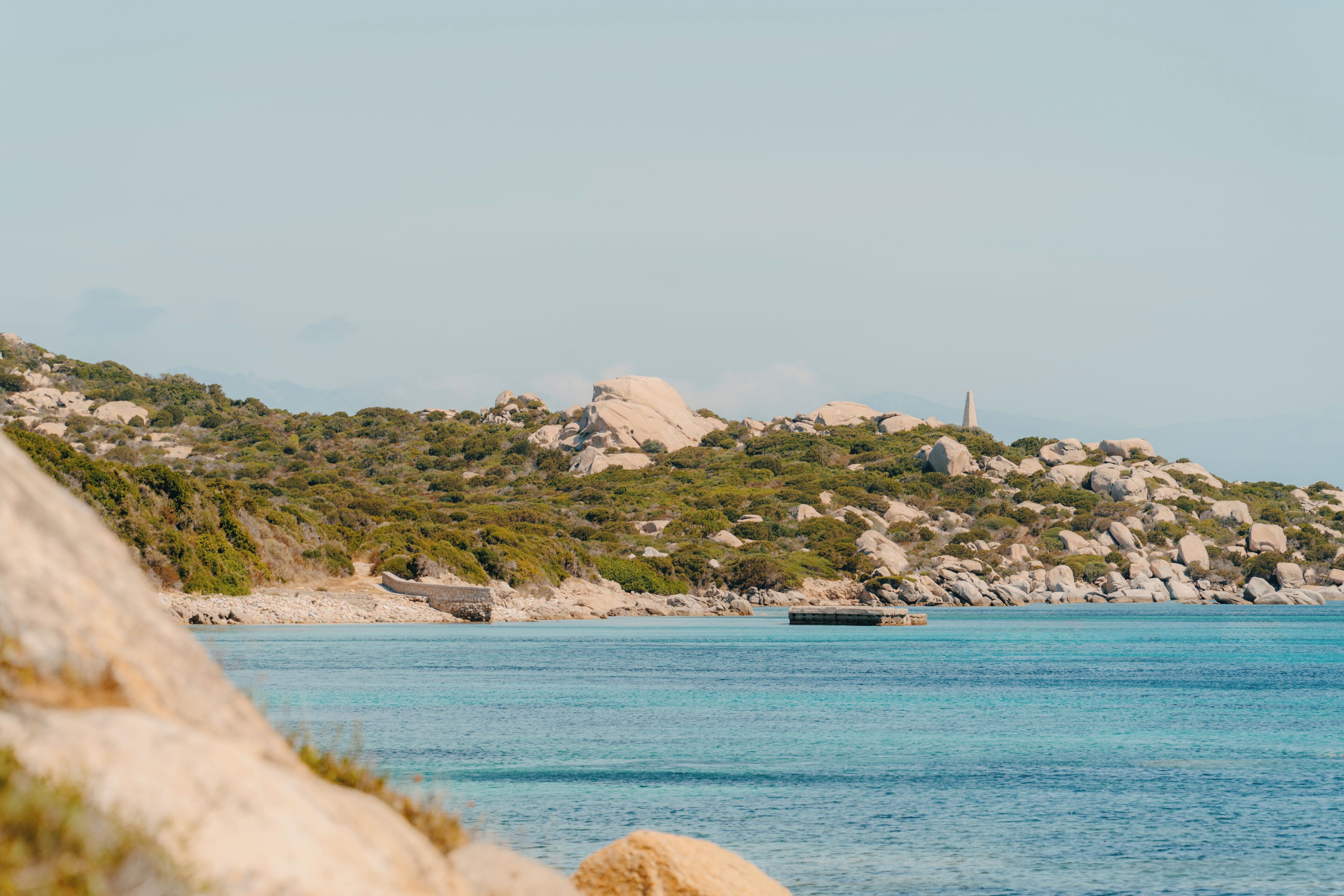 A coastal landscape with rocky terrain and a clear blue sea.
