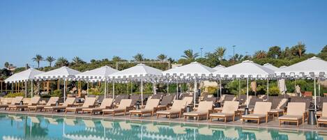 A poolside area with lounge chairs and umbrellas, surrounded by greenery and palm trees.