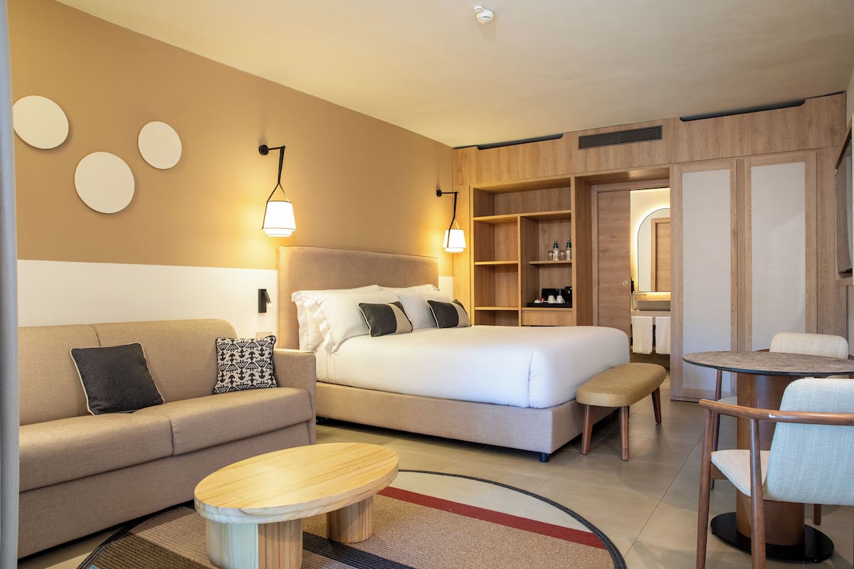 Une chambre d’hôtel comprenant un lit, un canapé, une table ronde, un petit banc et une armoire.