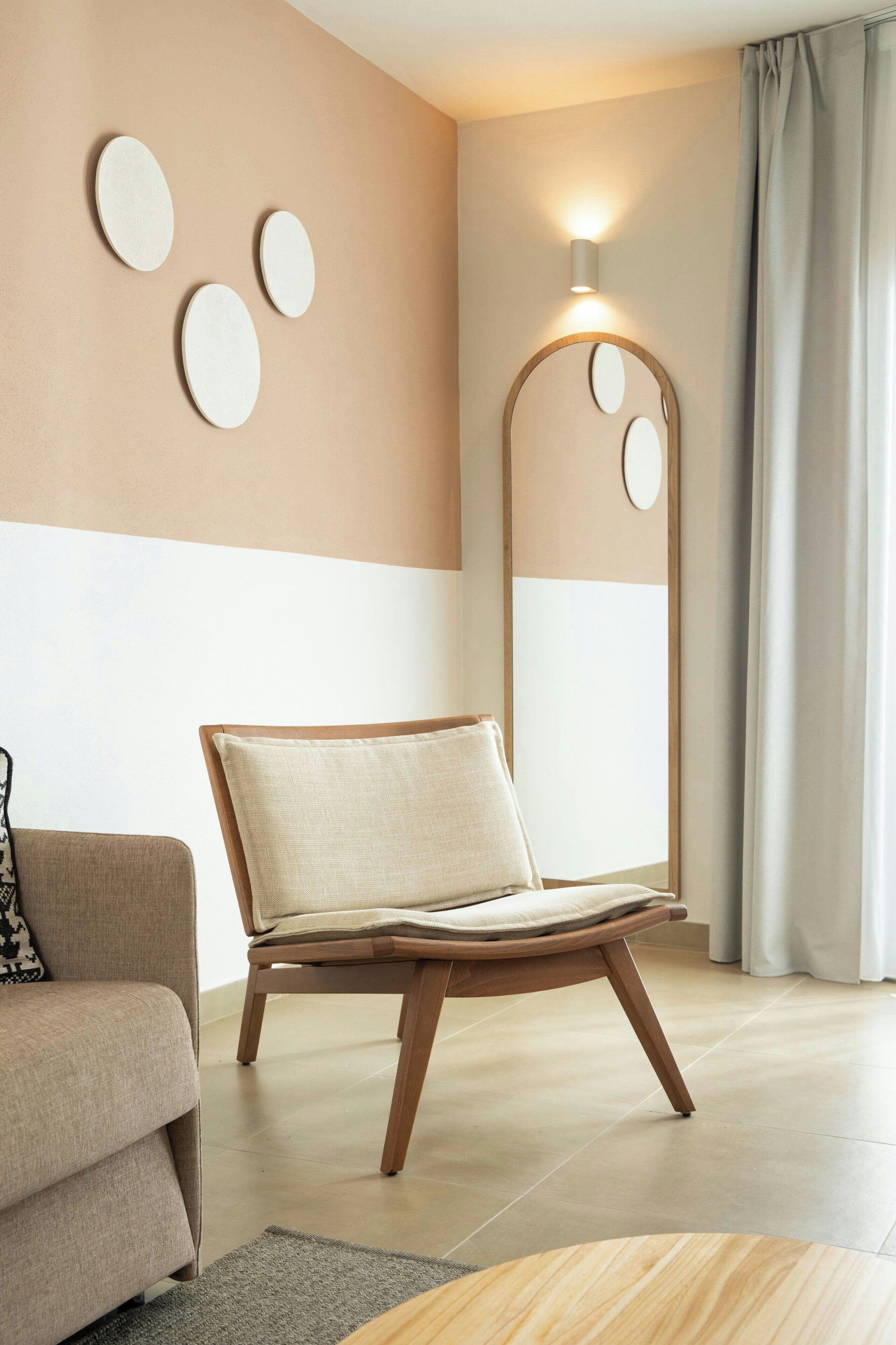 Een moderne woonkamer met een bank, een houten stoel, een spiegel en een wandlamp.