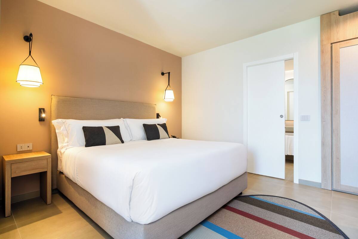 Une chambre d’hôtel avec un grand lit, deux lampes de chevet, une table de chevet et une porte donnant accès à une salle de bain.