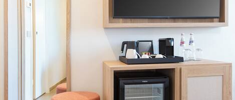 A hotel room with a large mirror, a flat-screen TV, a minibar, and a small refrigerator.