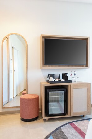 Een hotelkamer met een grote spiegel, een flatscreen televisie, een minibar en een kleine koelkast.