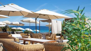 Espace extérieur aménagé avec des parasols, des meubles en osier et une vue sur la mer.