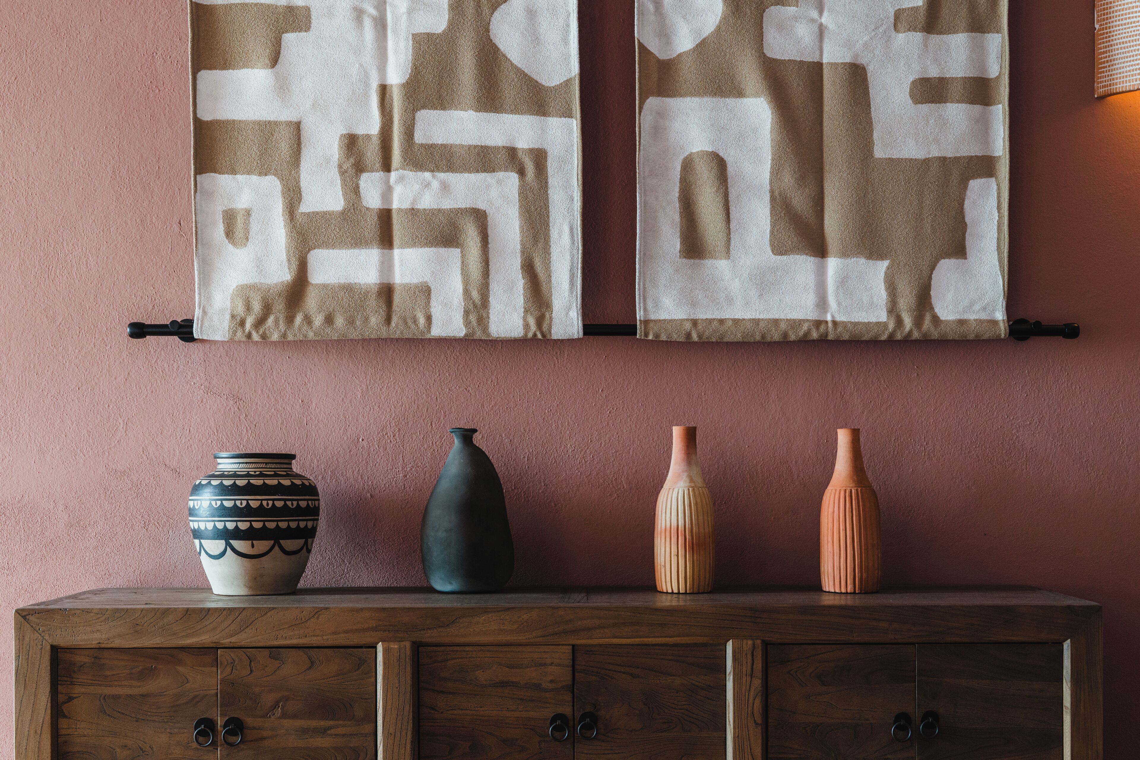 Een houten kastje met drie vazen en twee decoratieve handdoeken aan een muur.