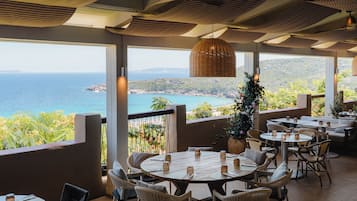 An outdoor dining area with tables and chairs, overlooking a coastal landscape.