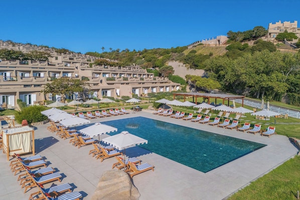 A resort with a large swimming pool surrounded by sun loungers and umbrellas.