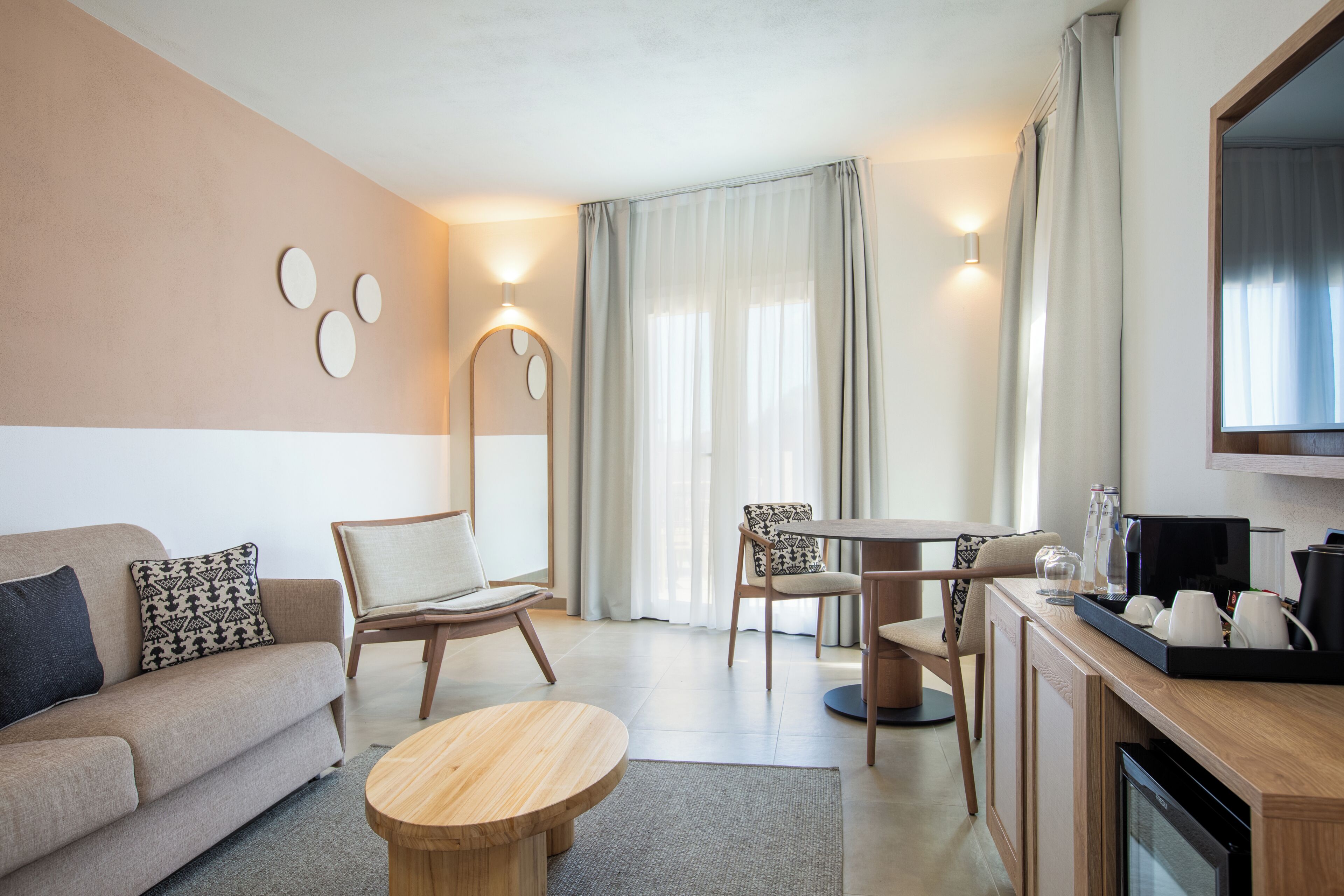 Quarto de hotel moderno com sofá, duas cadeiras, uma mesa de jantar, TV e cozinha.