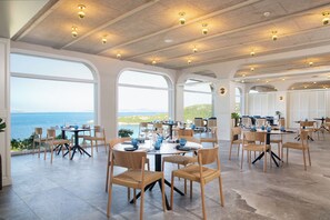 A spacious dining area with large windows, multiple tables, and chairs.
