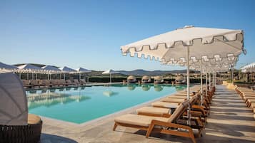 A pool area with lounge chairs and umbrellas, surrounded by mountains.