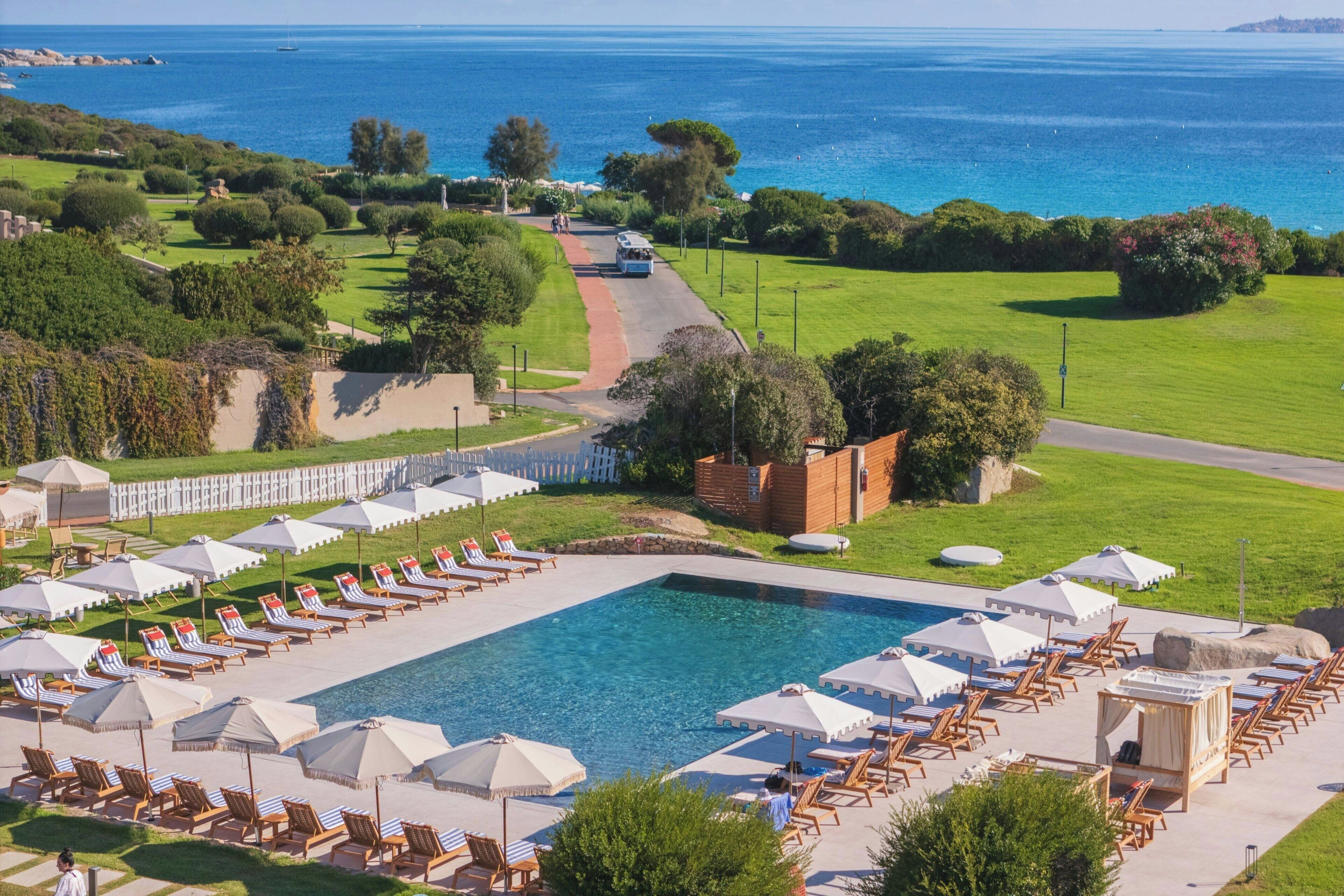 Un espace piscine agrémenté de chaises longues et de parasols, entouré de verdure et offrant une vue sur la mer.
