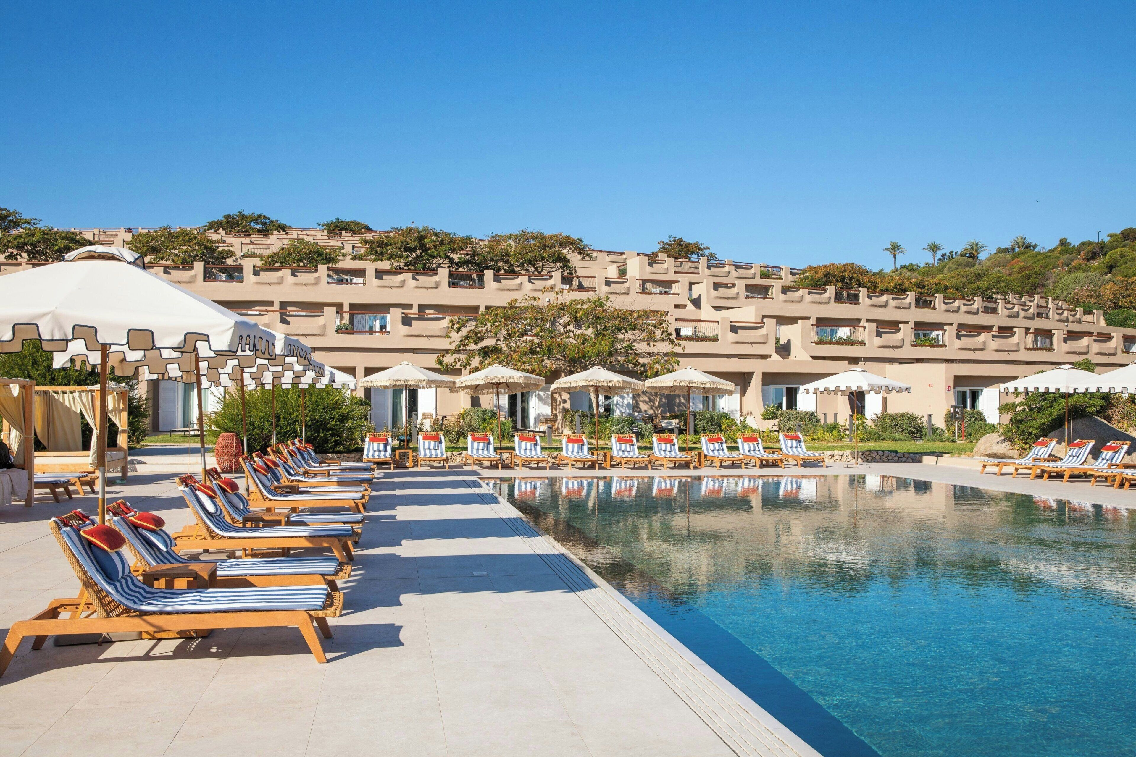 A poolside area with lounge chairs and umbrellas, a clear sky, and a building with multiple balconies.