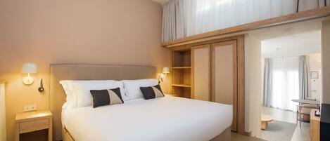A hotel room with a large bed, bedside lamps, a wardrobe, and a view of the dining area.