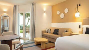Habitación de hotel con cama, sofá, mesa de comedor y una silla. Se ve el exterior a través de la puerta de vidrio.
