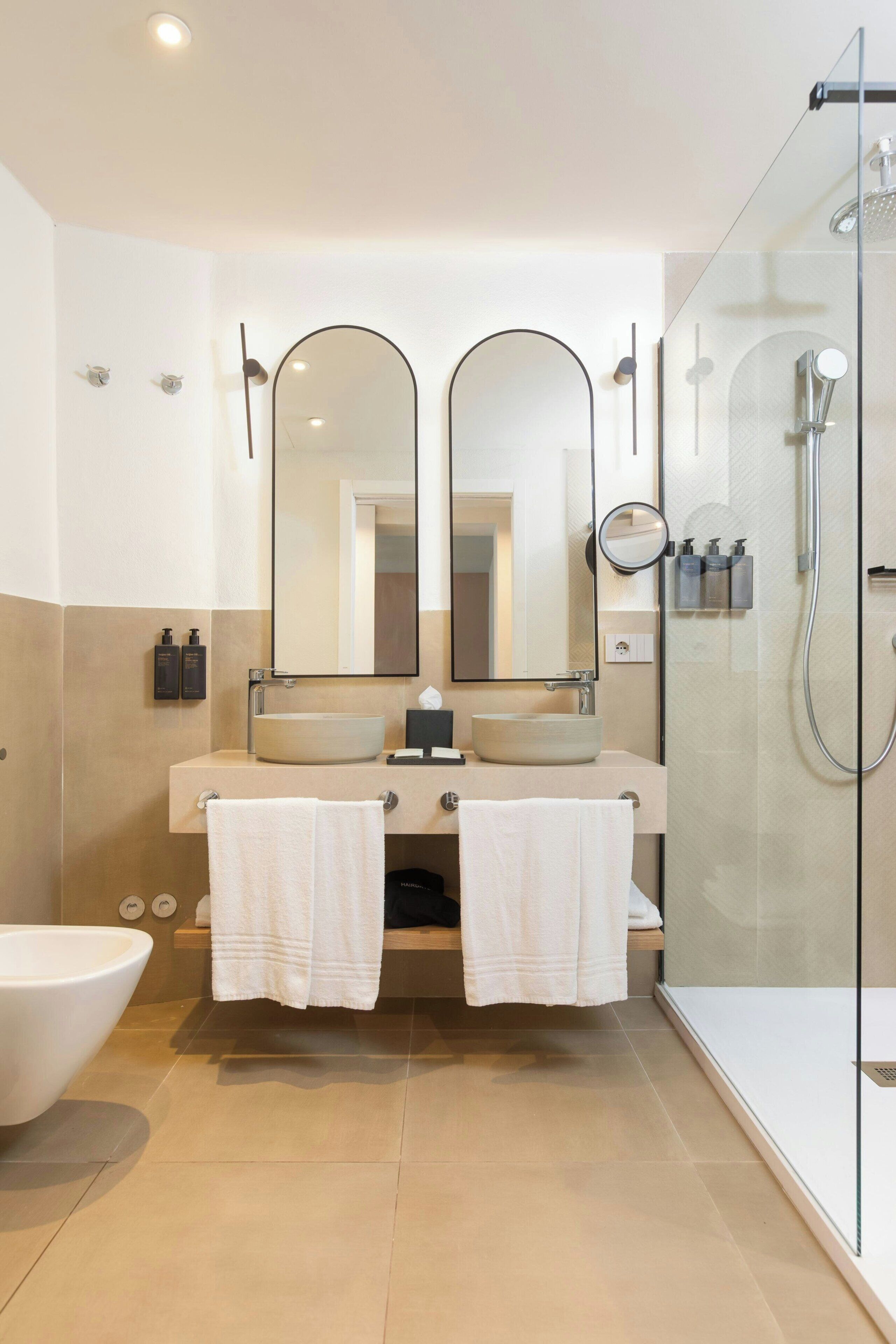 Un baño moderno con lavamanos doble, dos espejos, cabina de ducha de vidrio y un inodoro.