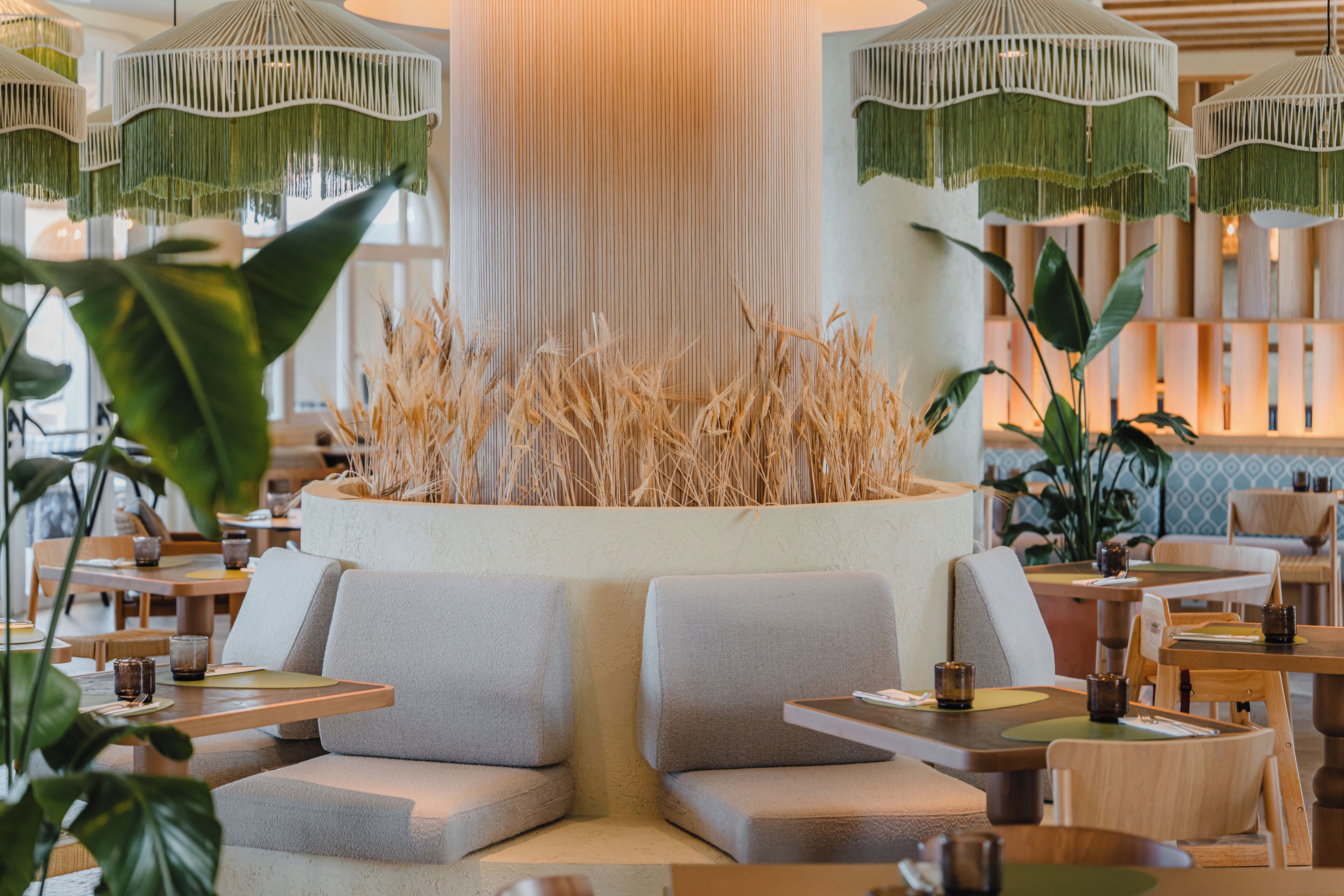 A modern interior with a central seating area, tables, and hanging green-fringed lights.