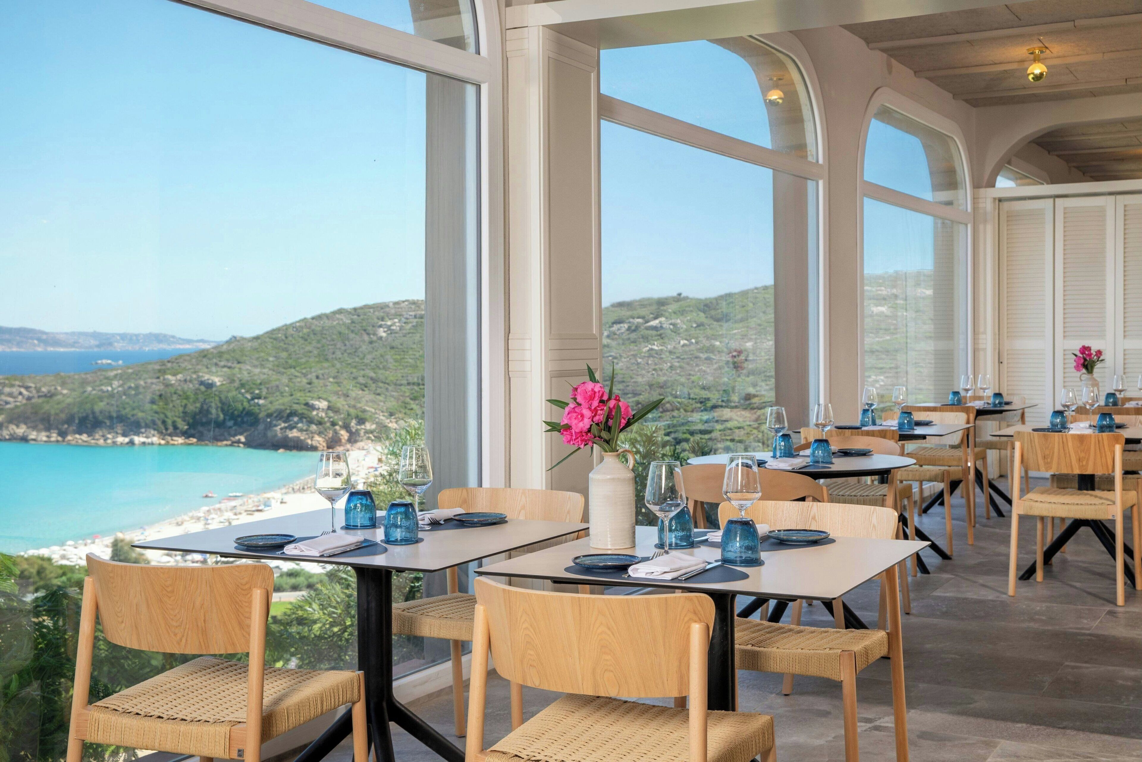 Un restaurant dont les tables sont dressées pour le service, offrant une vue sur un paysage côtier.