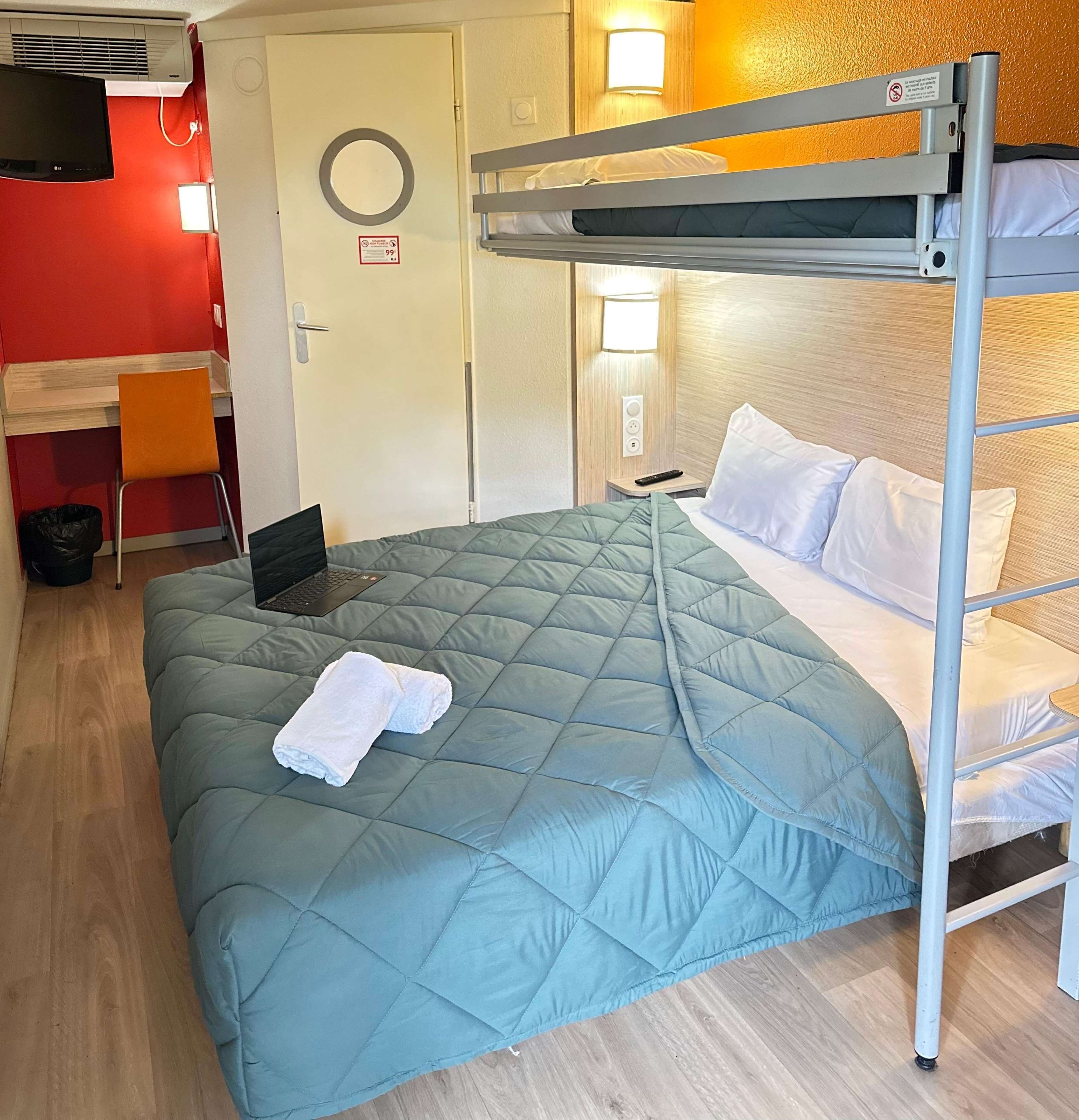Una cama litera con una computadora portátil en la cama inferior, una toalla blanca sobre la cama y un escritorio con una silla en la esquina.