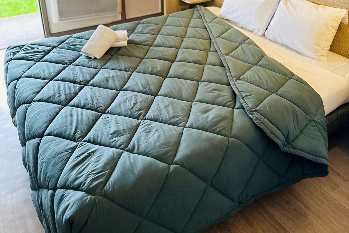 Una habitación de hotel con cama, mesita de noche, lámpara y cortina roja.