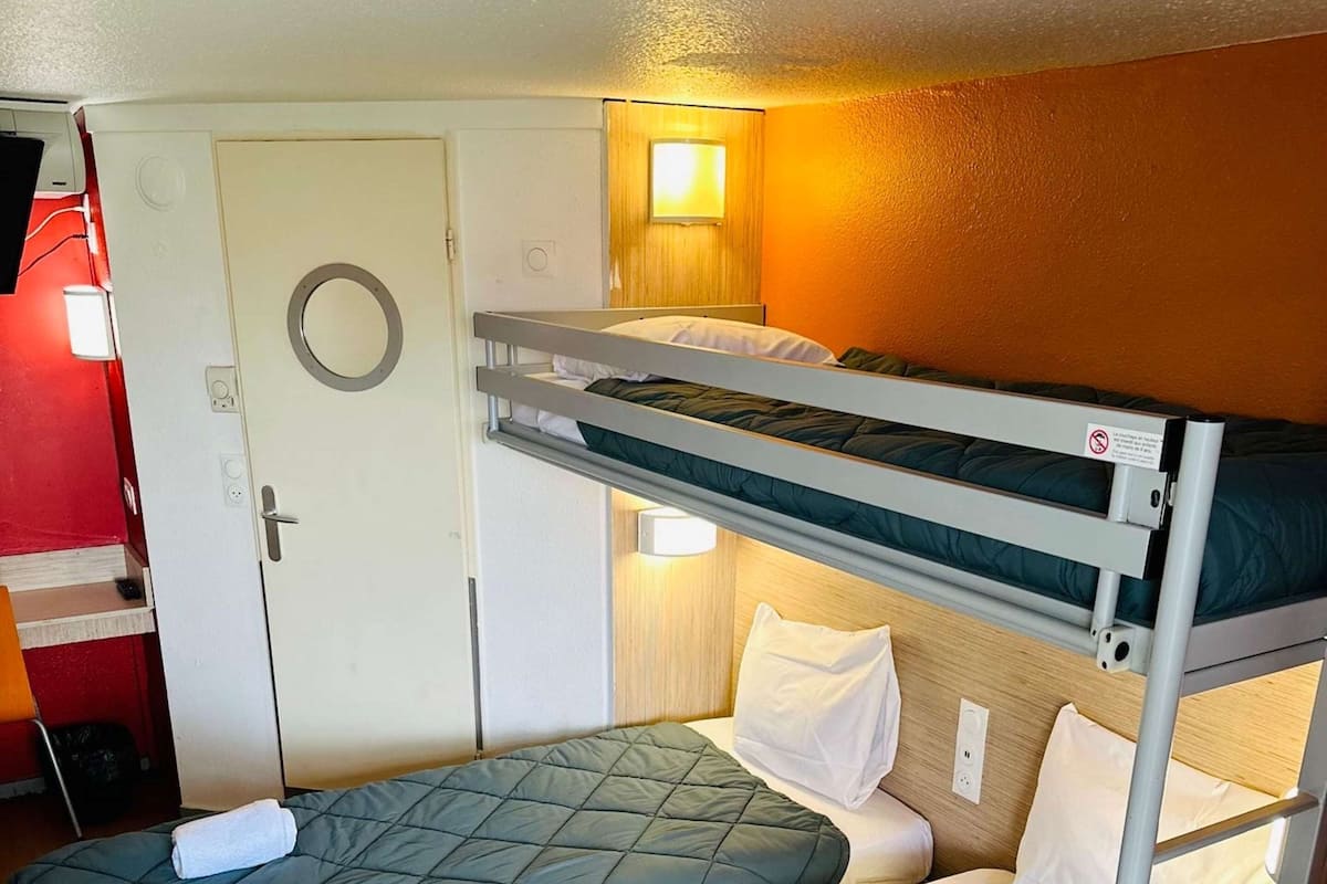 A bunk bed room with a door, a wall-mounted light, and a small window.