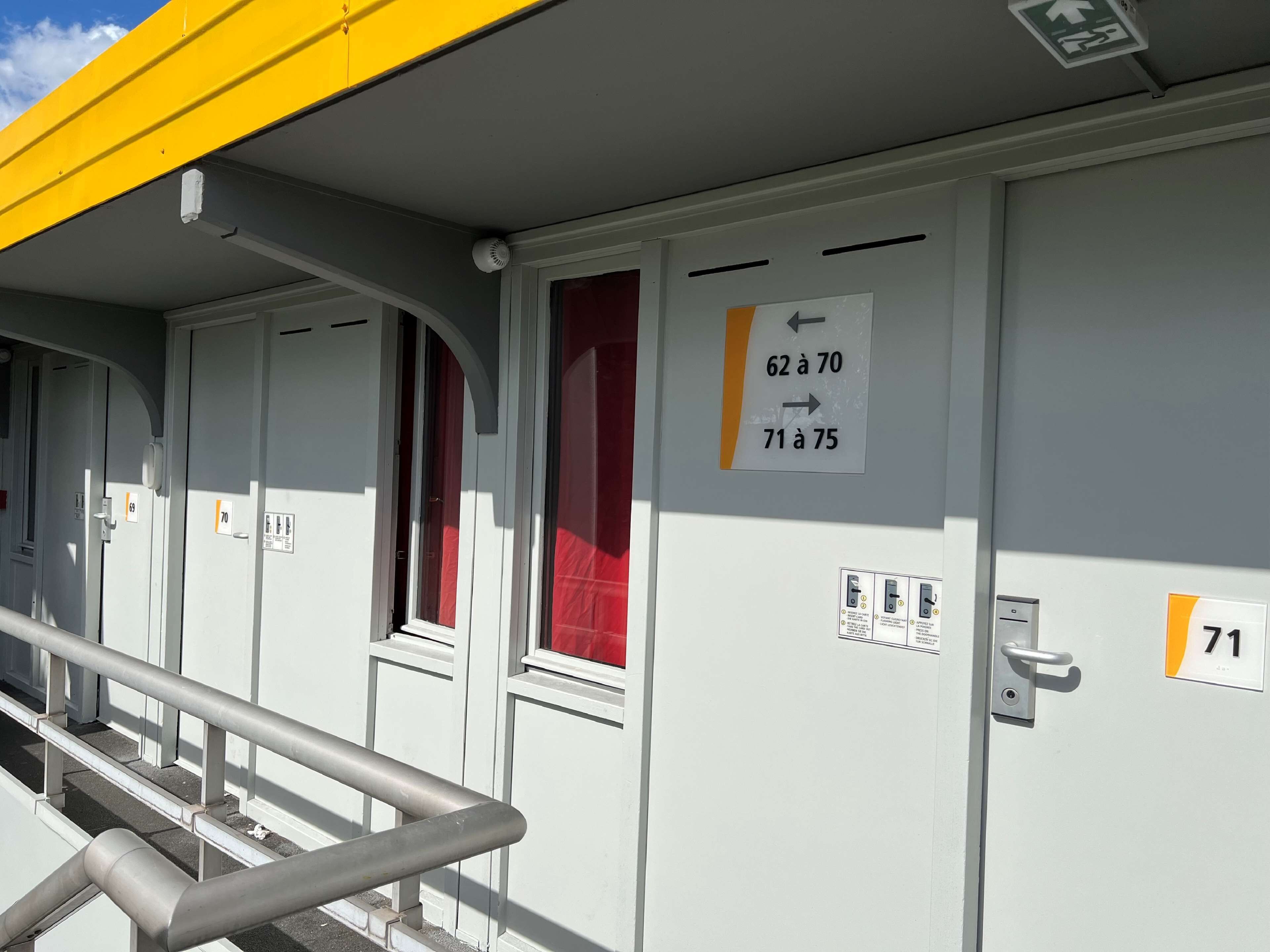 Una fila de habitaciones de hotel con puertas numeradas 69, 70, 71 y 75, y un cartel que indica las habitaciones del 62 al 70 y del 71 al 75.
