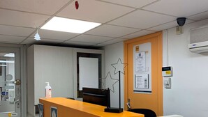A reception area with a desk, a computer, and a chair. There is a door to the left and a bulletin board on the wall. - Première Classe Dunkerque - Saint-Pol-Sur-Mer (Dunkirk)