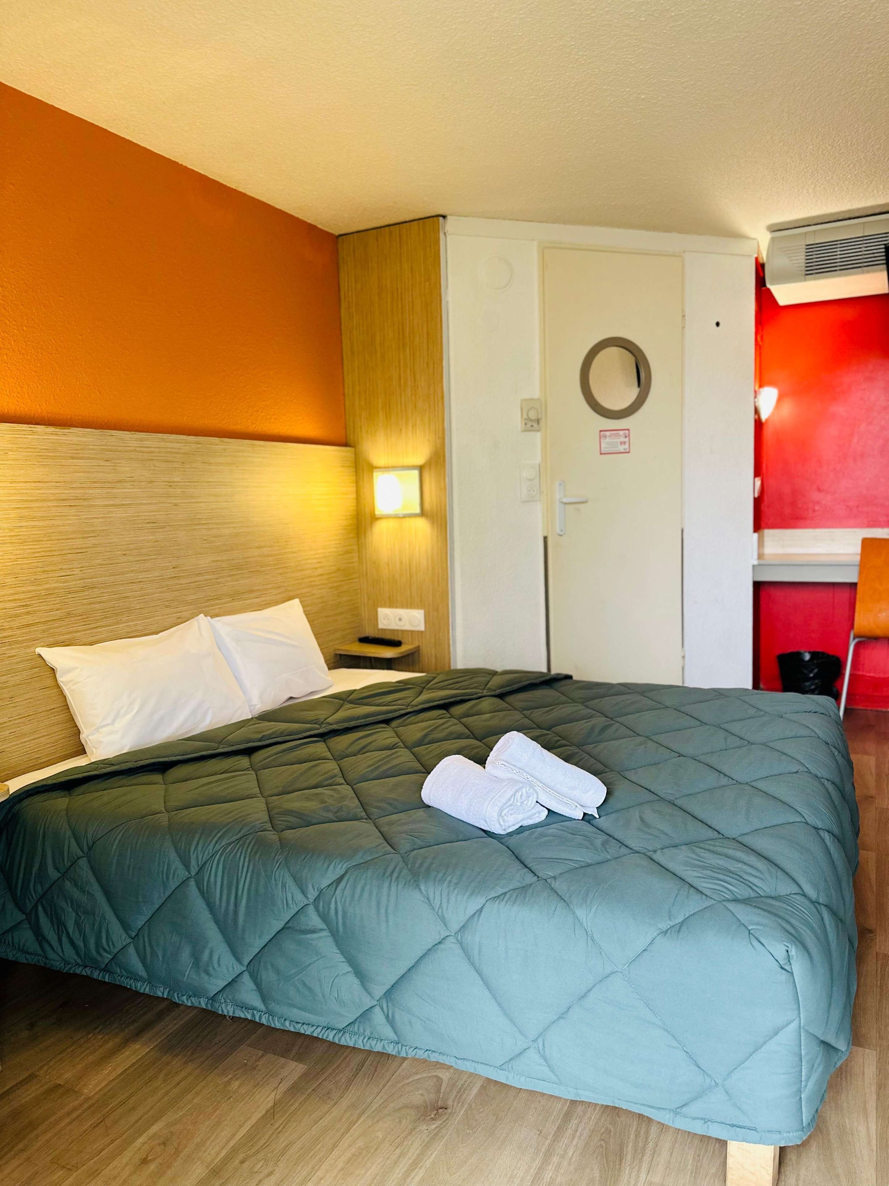 Una habitación de hotel con una cama, una mesita de noche, una lámpara, una puerta y una pared roja.
