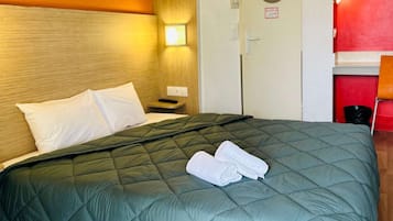 Una habitación de hotel con una cama, una mesita de noche, una lámpara, una puerta y una pared roja.