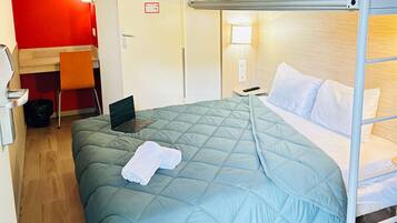 A bunk bed with a blue quilt, a desk with a laptop, a chair, and a red wall.